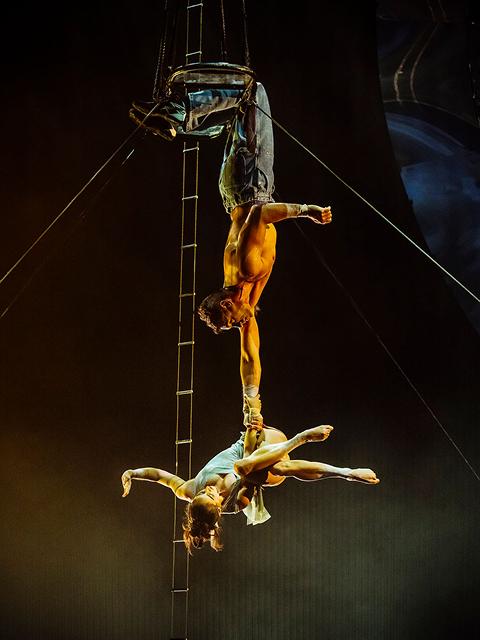 Cirque du Soleil aerial duo performs an inverted acrobatic routine suspended from a ladder high above the stage.